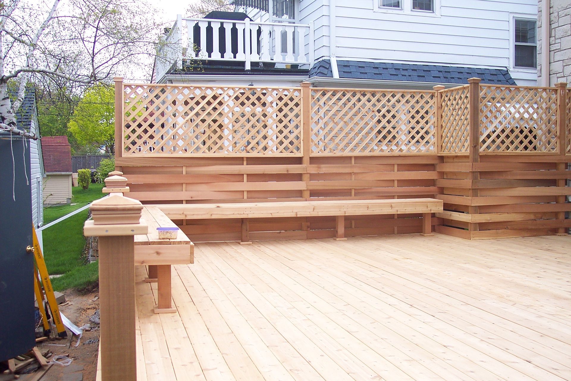 Wooden backyard deck with lattice railing and steps beside a house, showing a small table and posts.