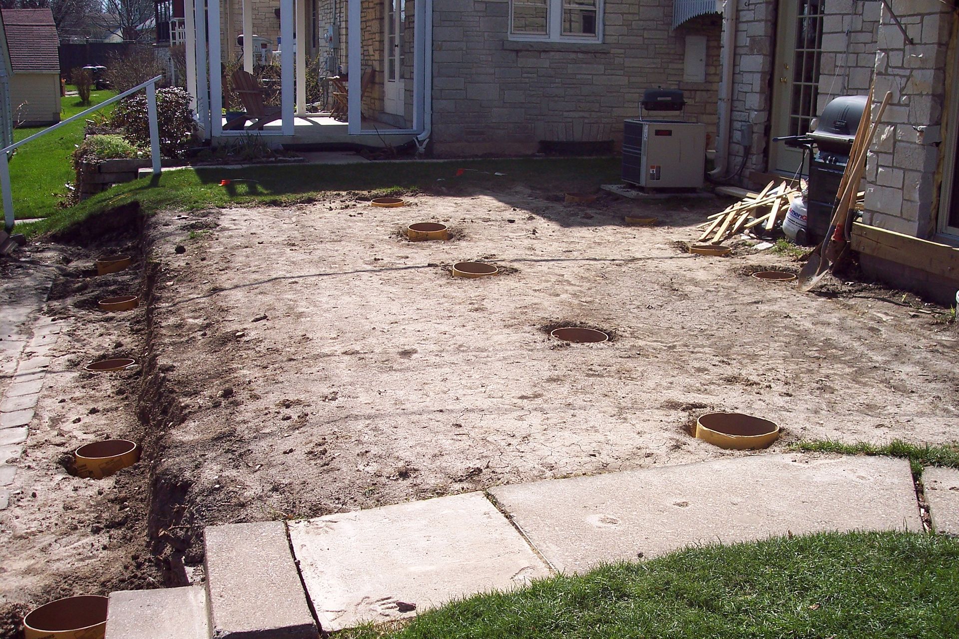 Backyard with a dirt patch, stone edging, and a brick house patio in the background