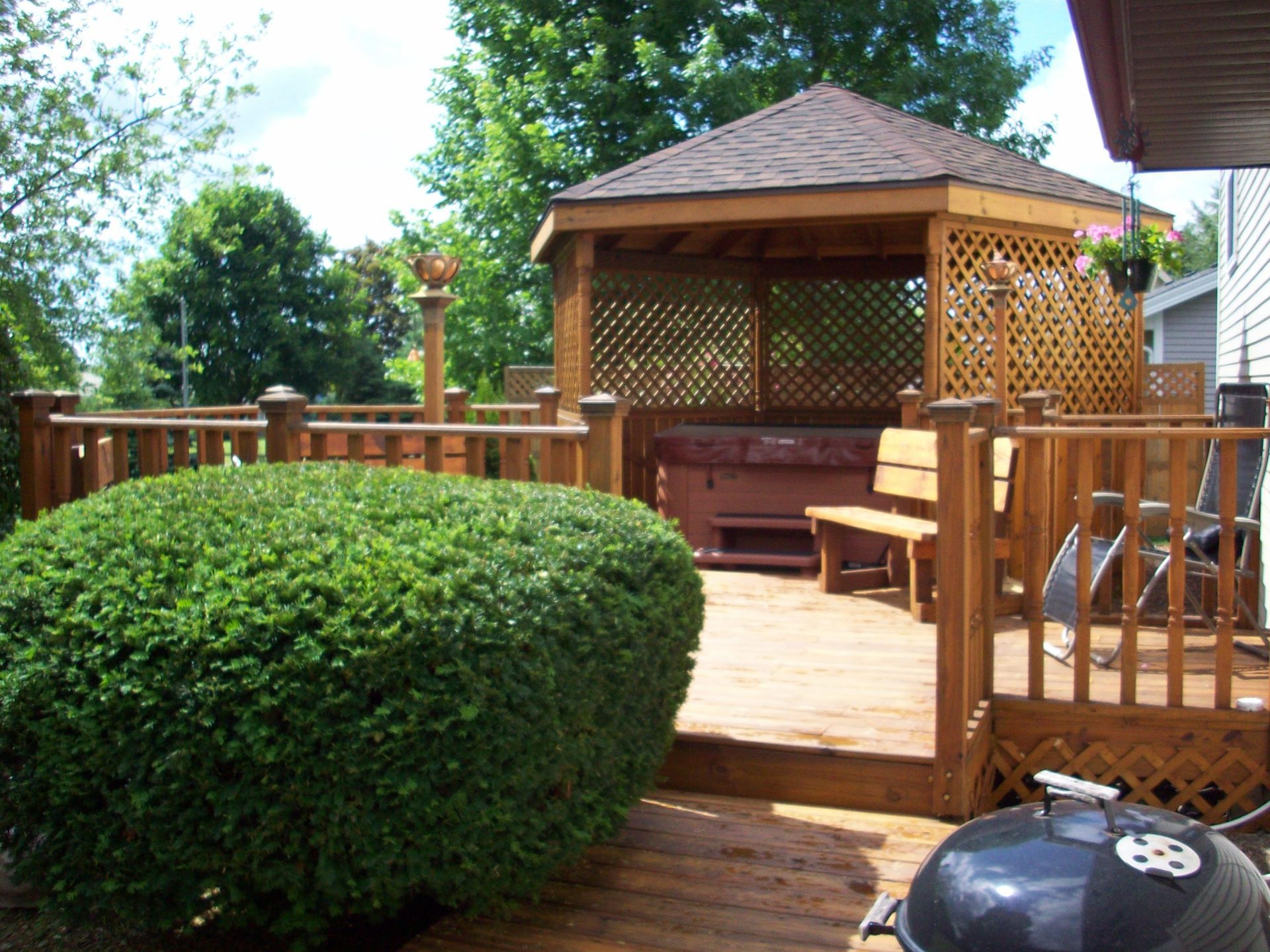 Wooden deck with gazebo, benches, and lush green shrubs in a sunny backyard
