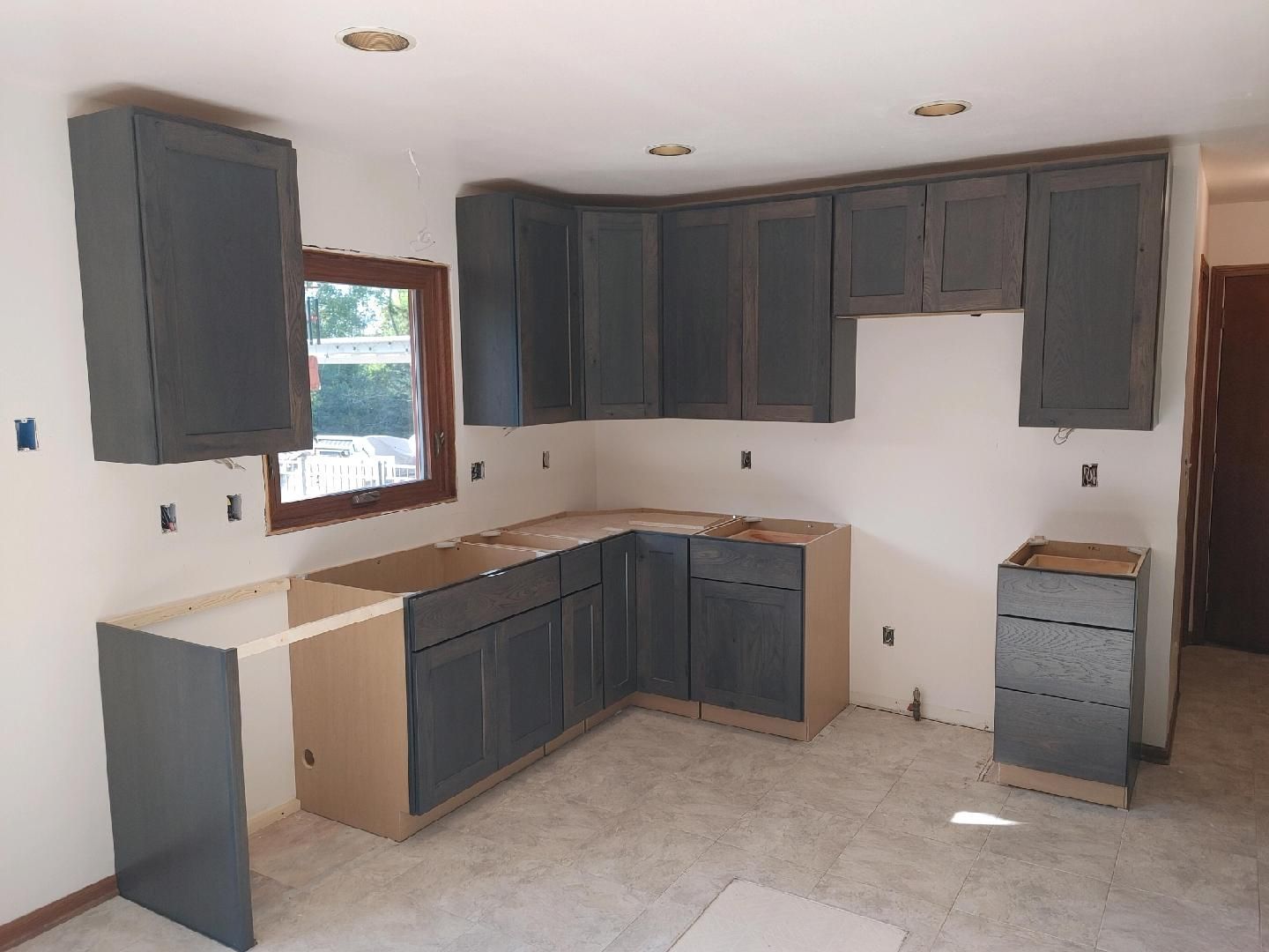 Unfinished kitchen with dark cabinets, beige countertops, and a window over the sink.