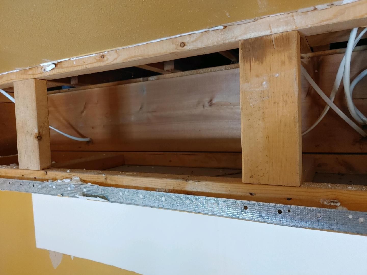 Damaged wall opening with exposed wooden studs, wiring, and a broken lower edge