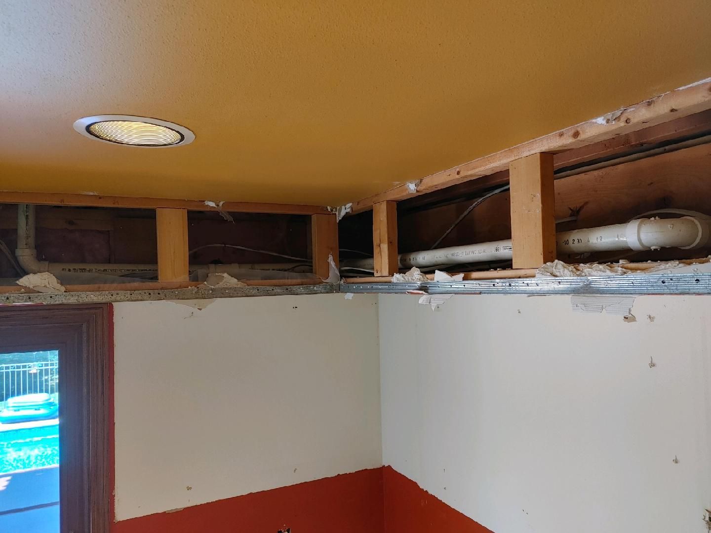 Partially renovated room with exposed ceiling beams, white walls, and a red lower wall section.