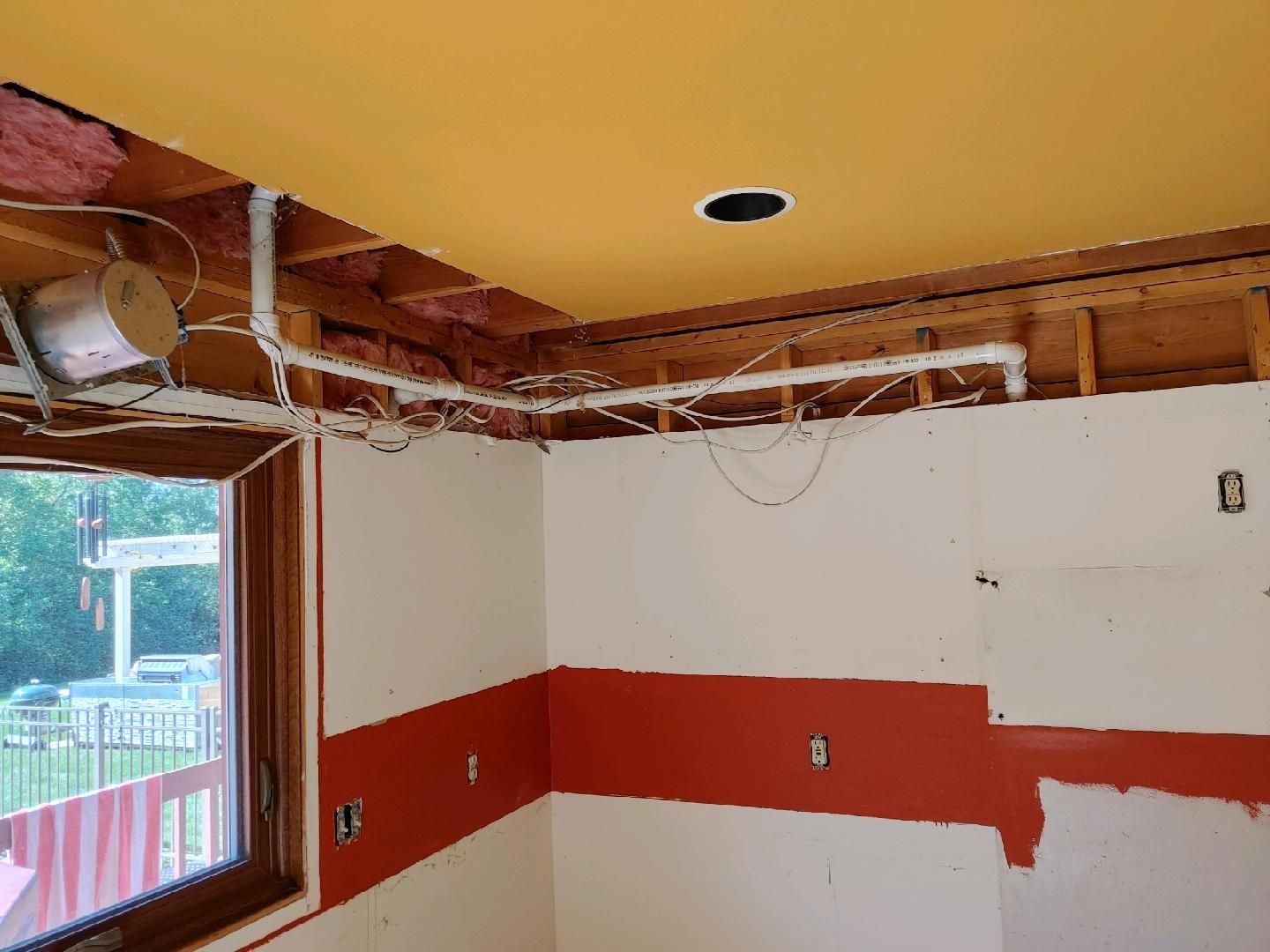 Partially renovated room with exposed ceiling, white walls, and a red horizontal stripe by a window