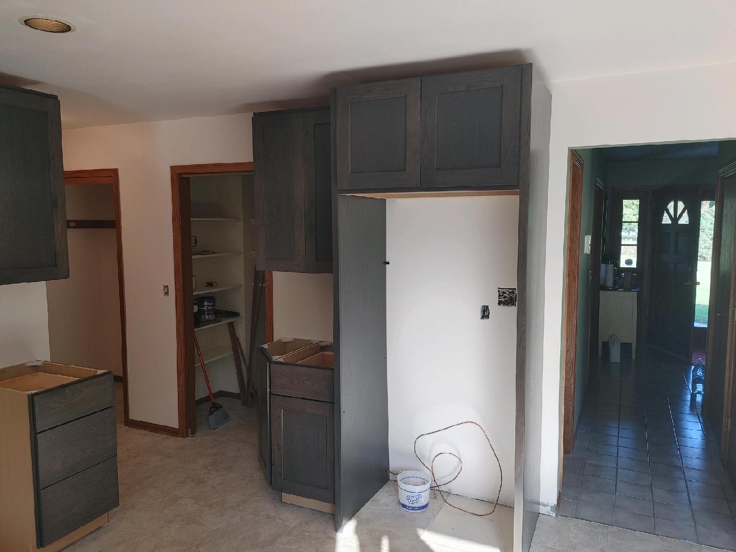 Small kitchen with dark cabinets, white fridge, and tiled floor opening to a hallway.