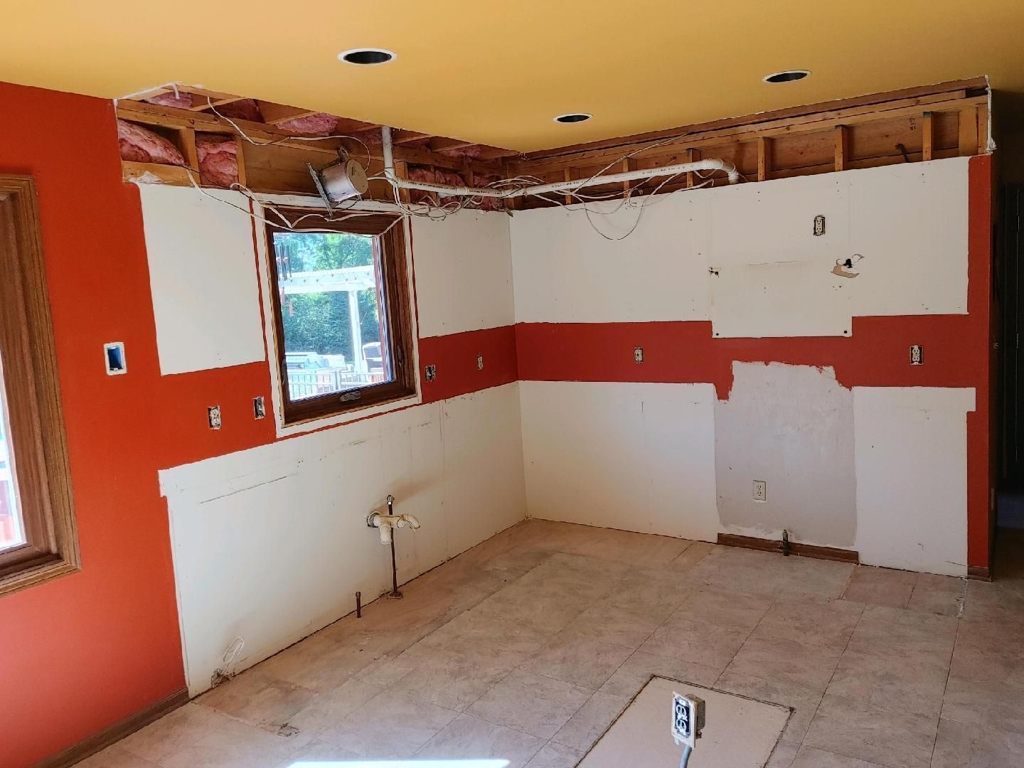 Partially renovated kitchen with orange and white walls, exposed ceiling, and unfinished tile floor