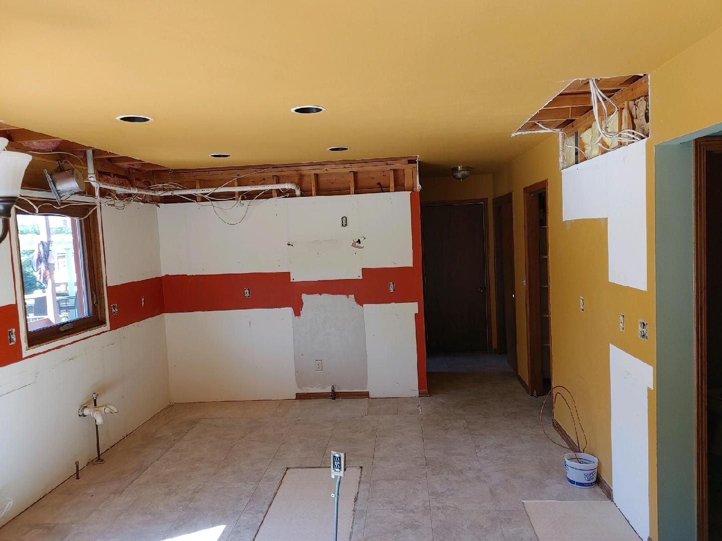 Partially renovated room with exposed ceiling, white walls, red stripe, and unfinished doorway
