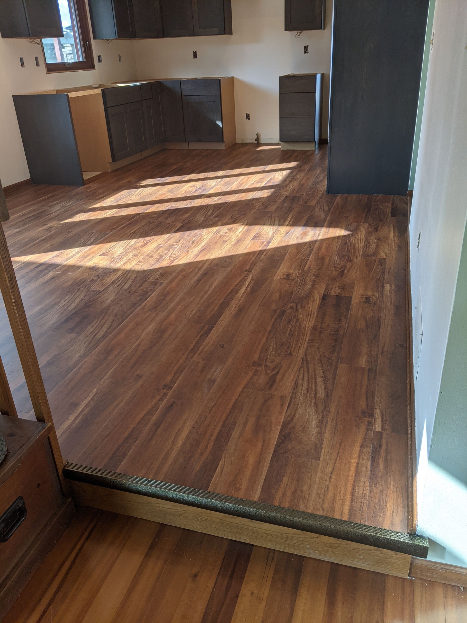 Empty kitchen with wood-look flooring and sunlight streaming across the floor