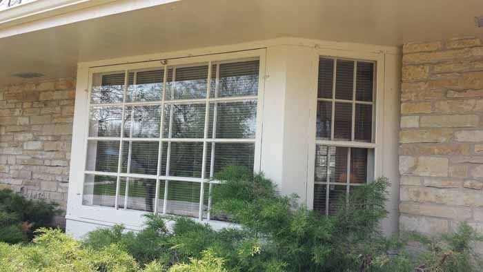 Stone house exterior with large window, narrow side window, and green shrubs below