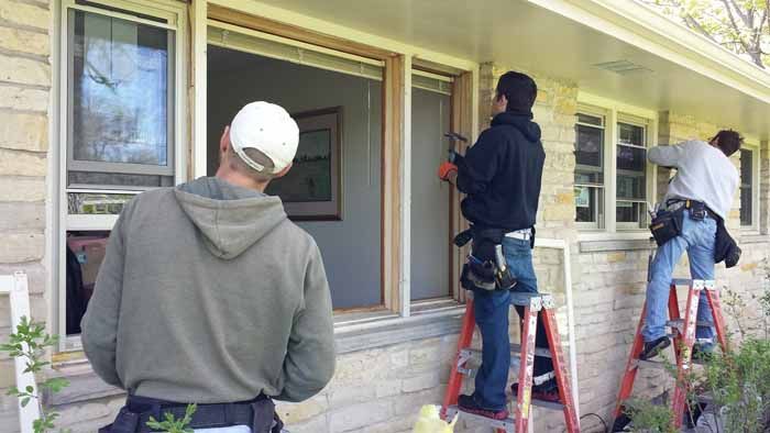 Three workers on ladders painting the exterior of a house porch and window trim