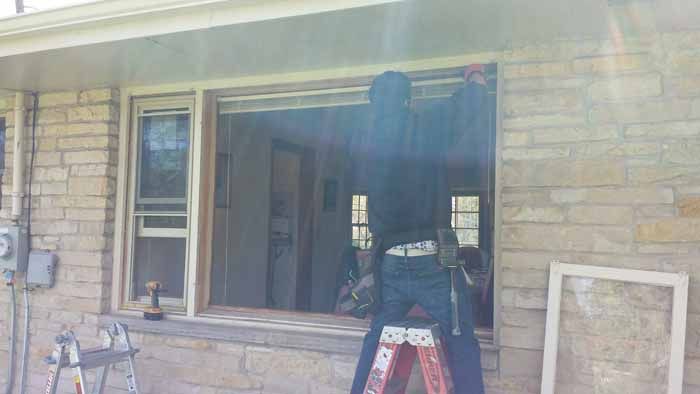 Person standing on a ladder installing a window in a stone house exterior