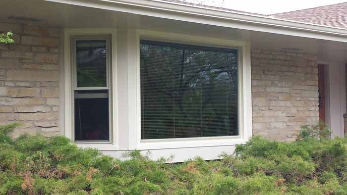 Stone house facade with large white-framed window and green shrubs below