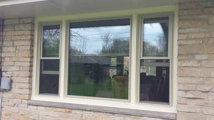 Three-pane white-framed window set in a stone exterior wall, with reflections visible in the glass