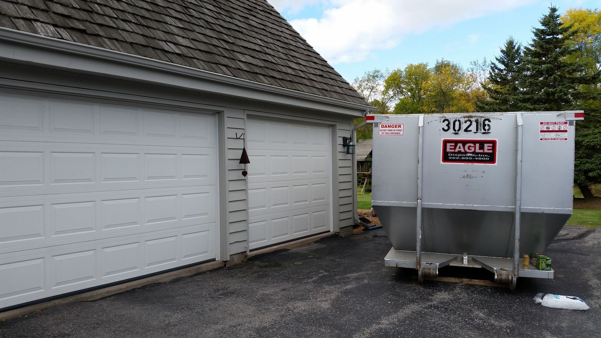 White garage beside a silver EAGLE dumpster on a driveway under a partly cloudy sky