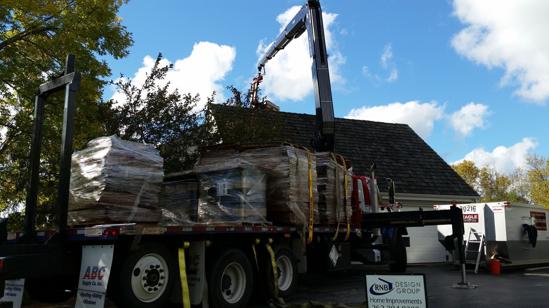 Flatbed truck loaded with wrapped cargo, parked outdoors under a blue sky.