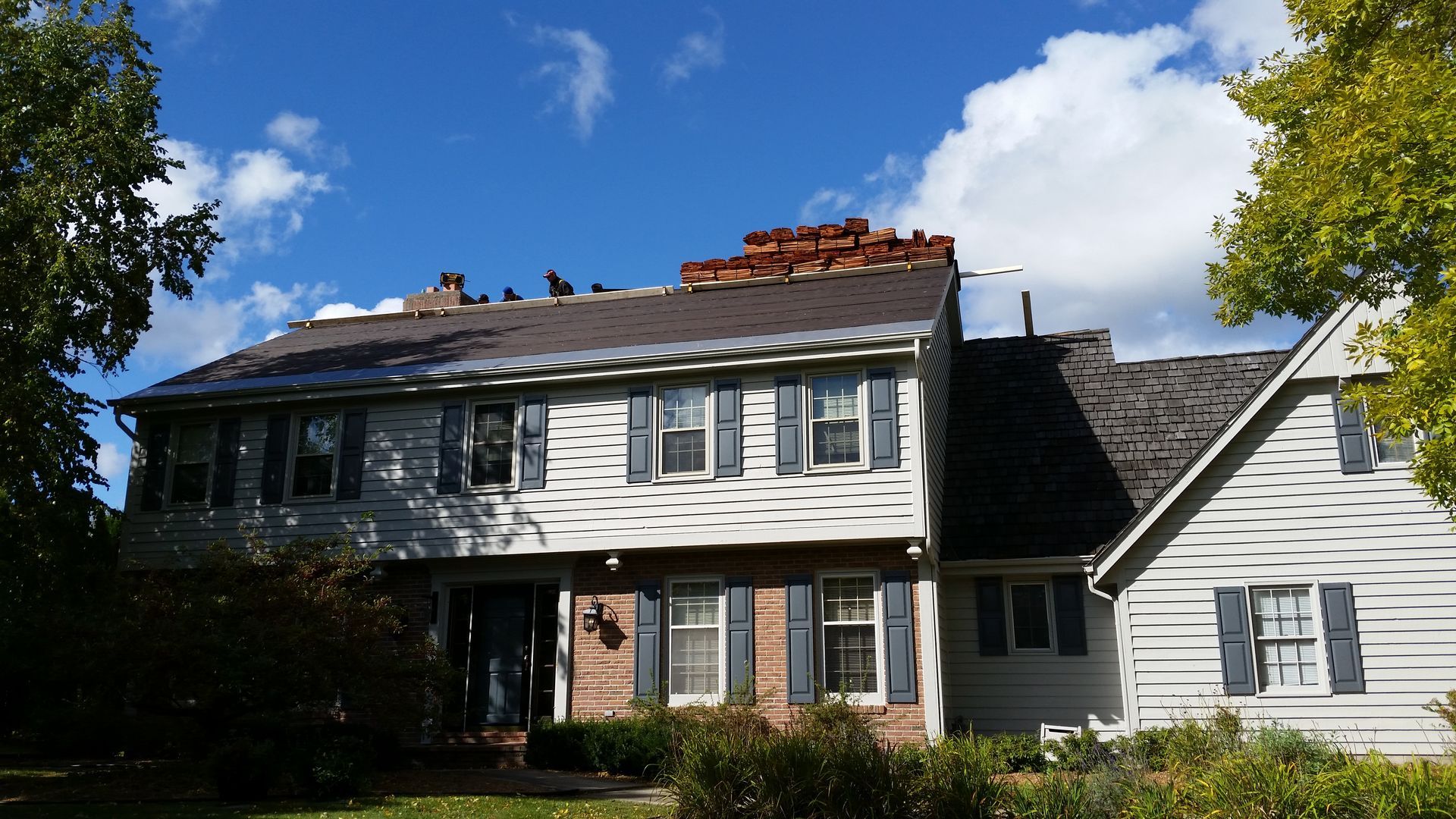 Two-story gray house with white trim and a brick chimney under a blue sky