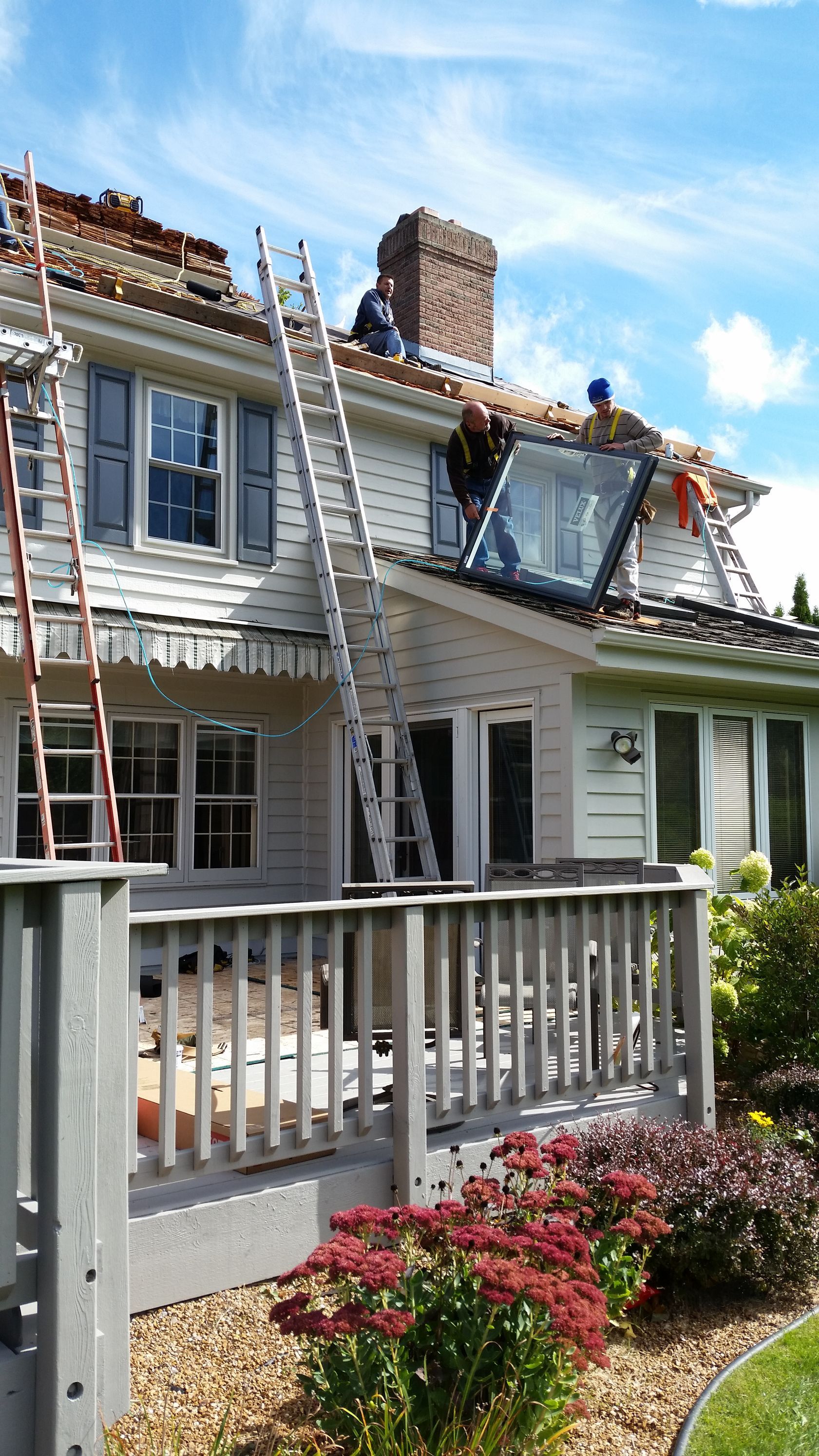 Workers repairing the roof of a white house with ladders and scaffolding under a blue sky