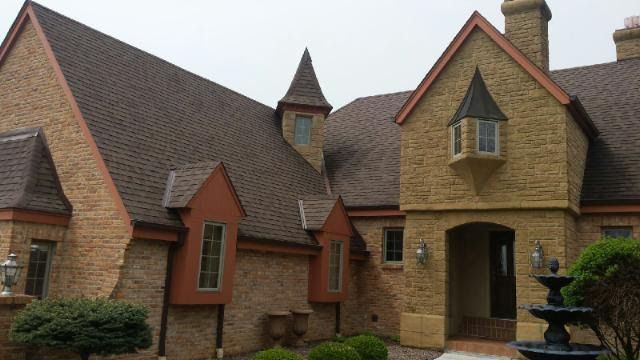 Brick and stucco house with steep shingled roofs and arched entryway