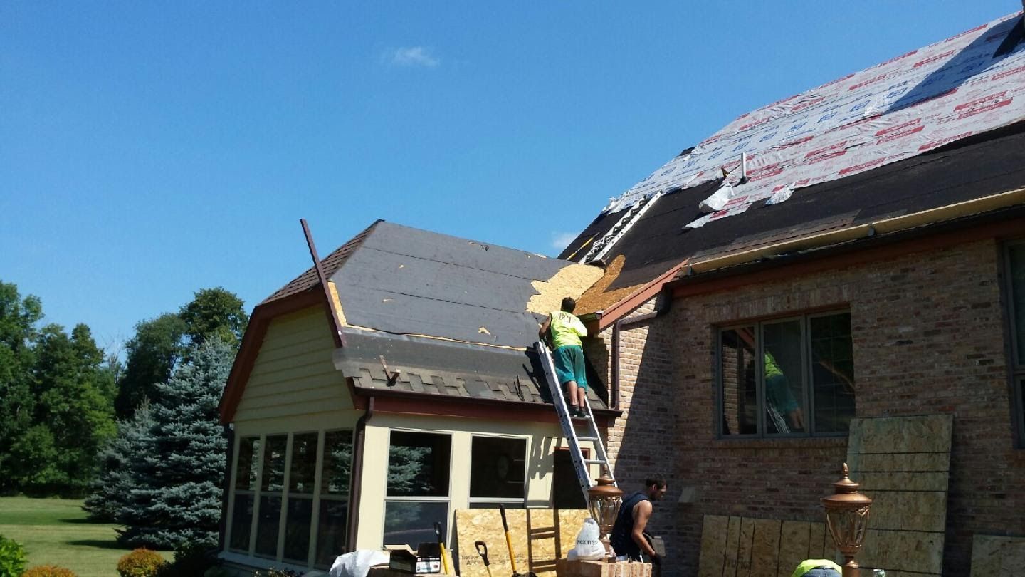 Workers repairing a roof on a brick and wood house under a clear blue sky