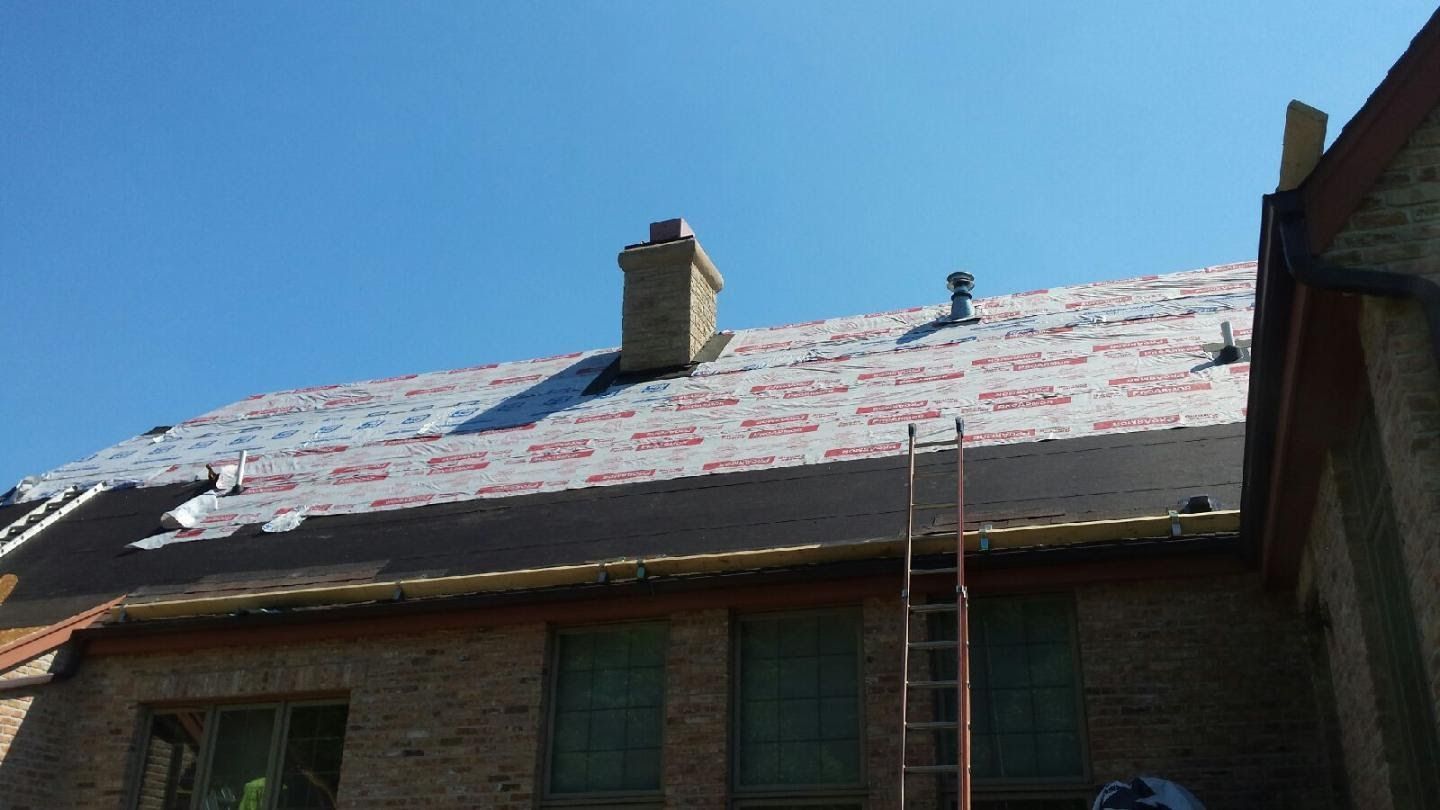 Roofer working on a house roof covered with white underlayment, with a ladder against the wall