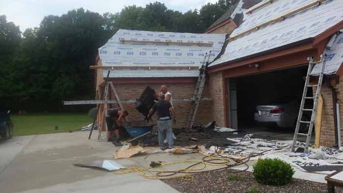 Workers install roof sheathing and scaffolding on a brick house during a home renovation.