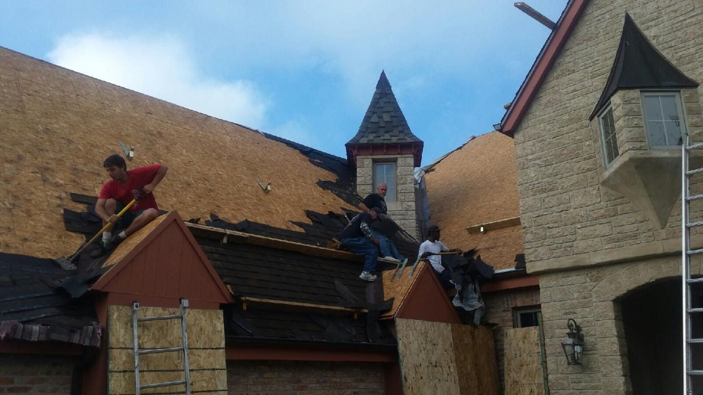 Workers repairing a steep roof on a stone building under a blue sky