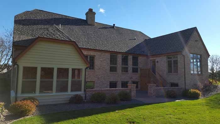 Suburban brick house with gabled roof, large windows, and a green lawn in front.