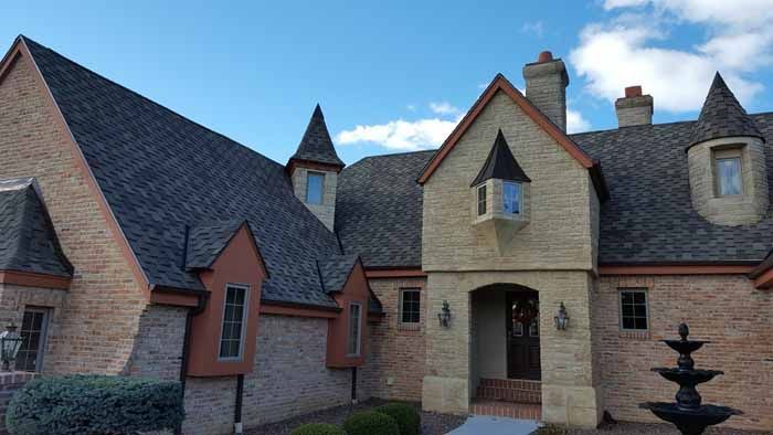 Charming stone courtyard with steep slate roofs, arched doorway, and a black fountain under a blue sky