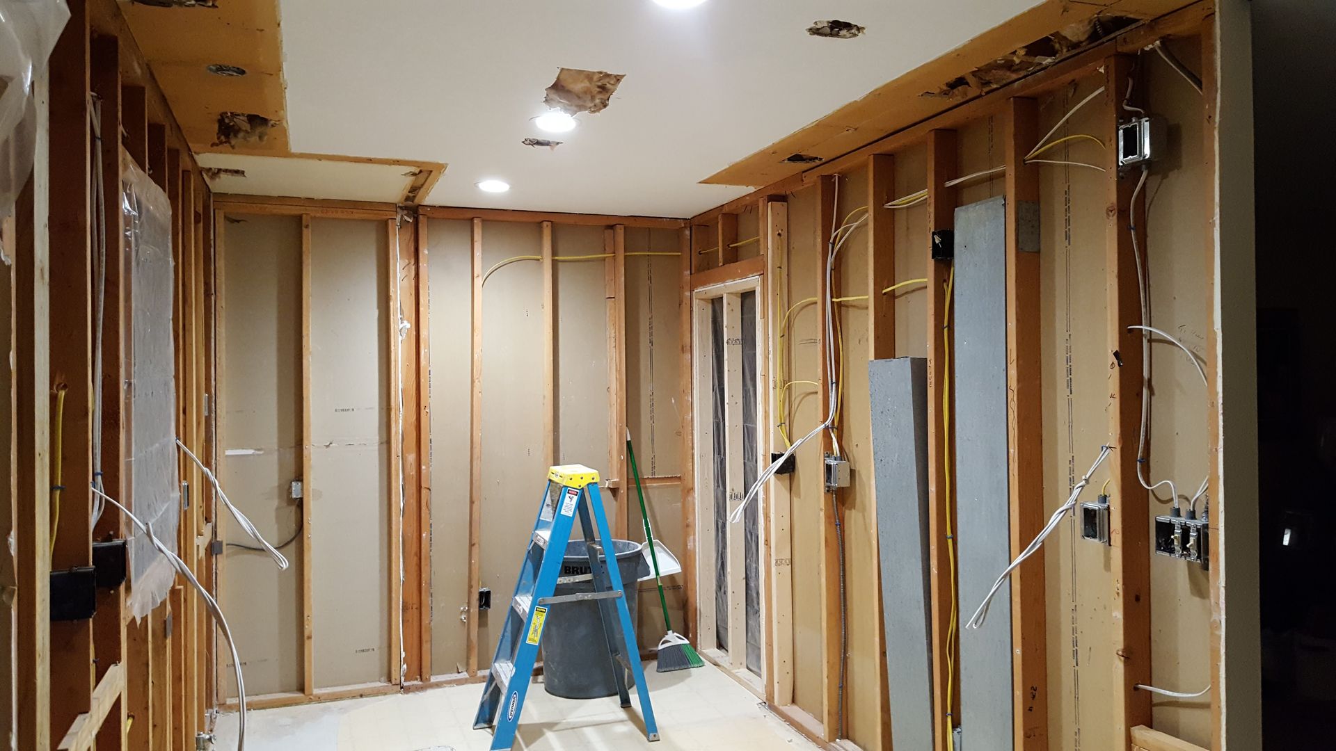 Partially renovated room with exposed wall framing, ladder, and recessed ceiling lights