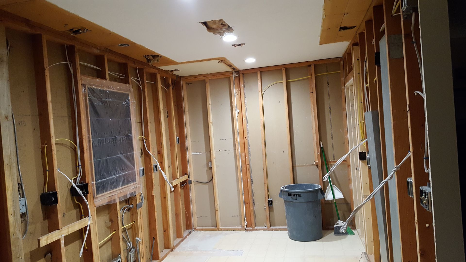 Interior room under renovation with exposed wall studs, bucket on floor, and a window on the left.