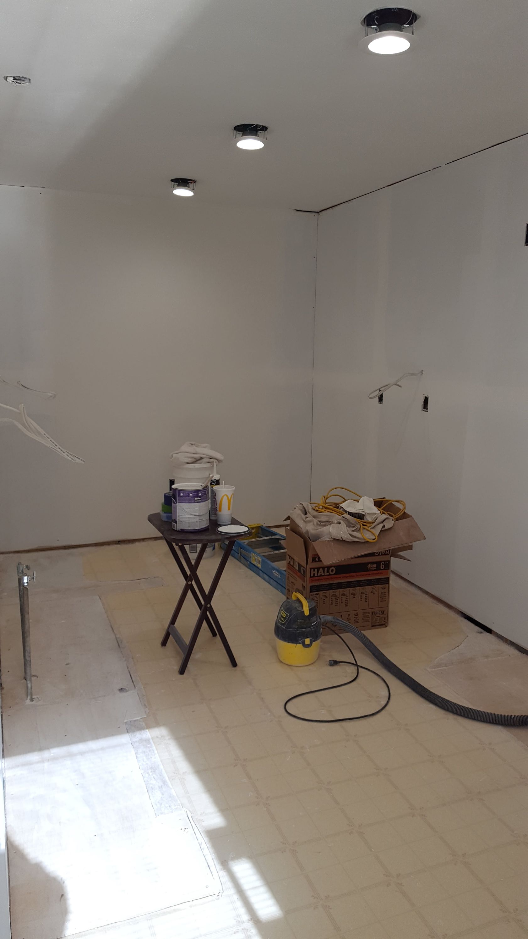 Empty room under renovation with white walls, tiled floor, tools, and ceiling lights