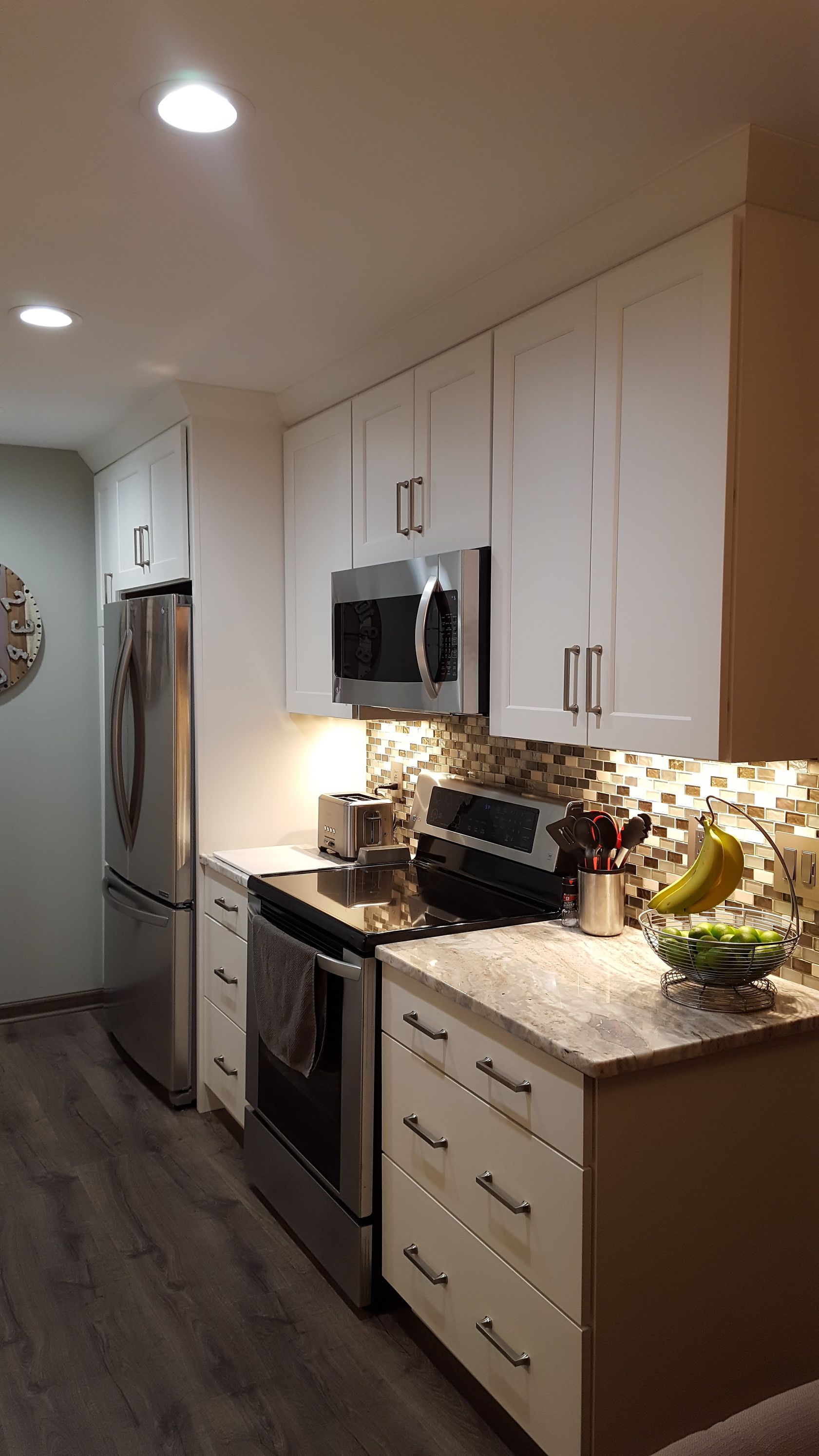Modern kitchen with white cabinets, granite counters, stainless appliances, and a tiled backsplash in warm lighting