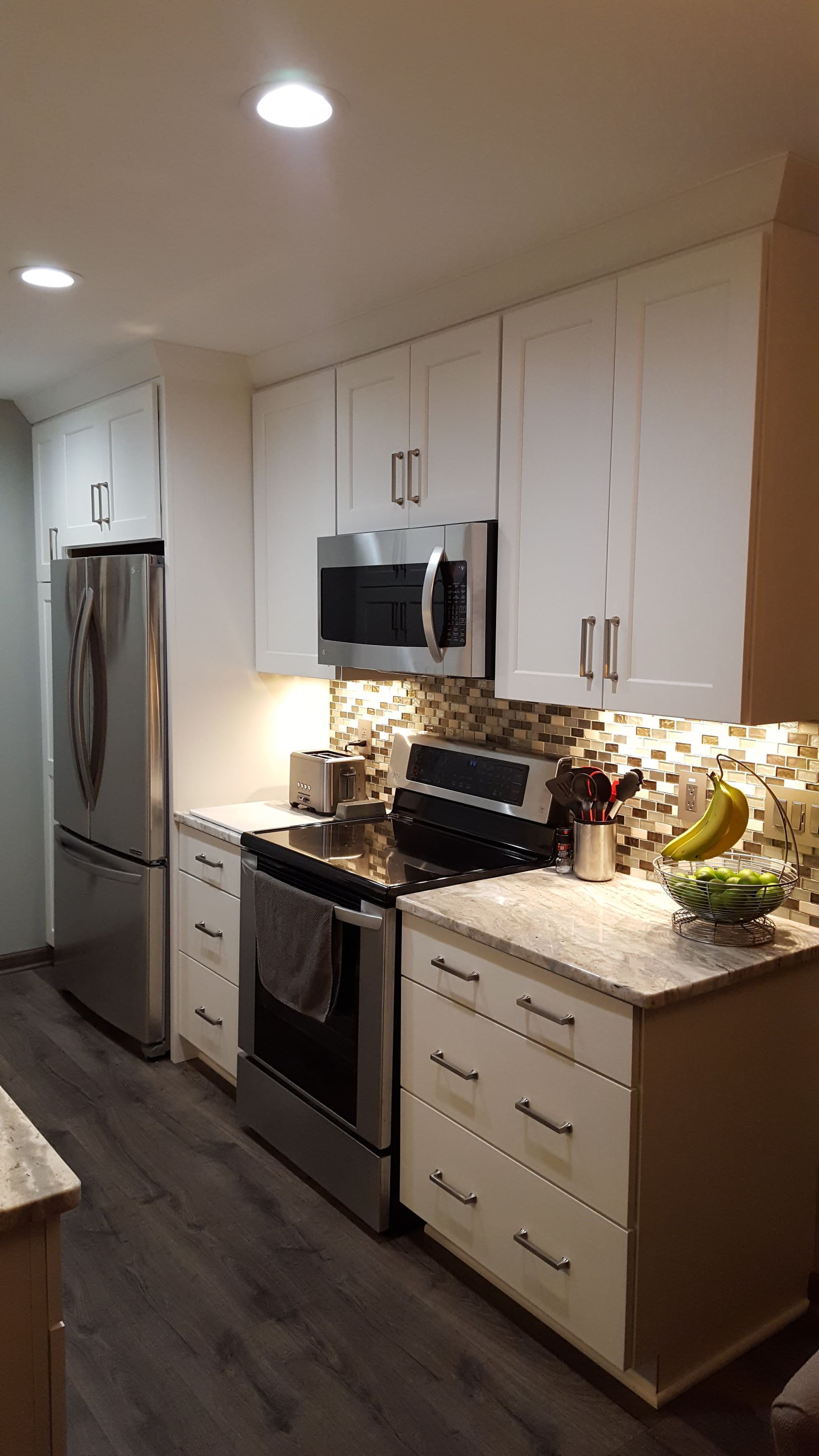Modern kitchen with white cabinets, stainless steel appliances, and granite countertops along a narrow hallway.