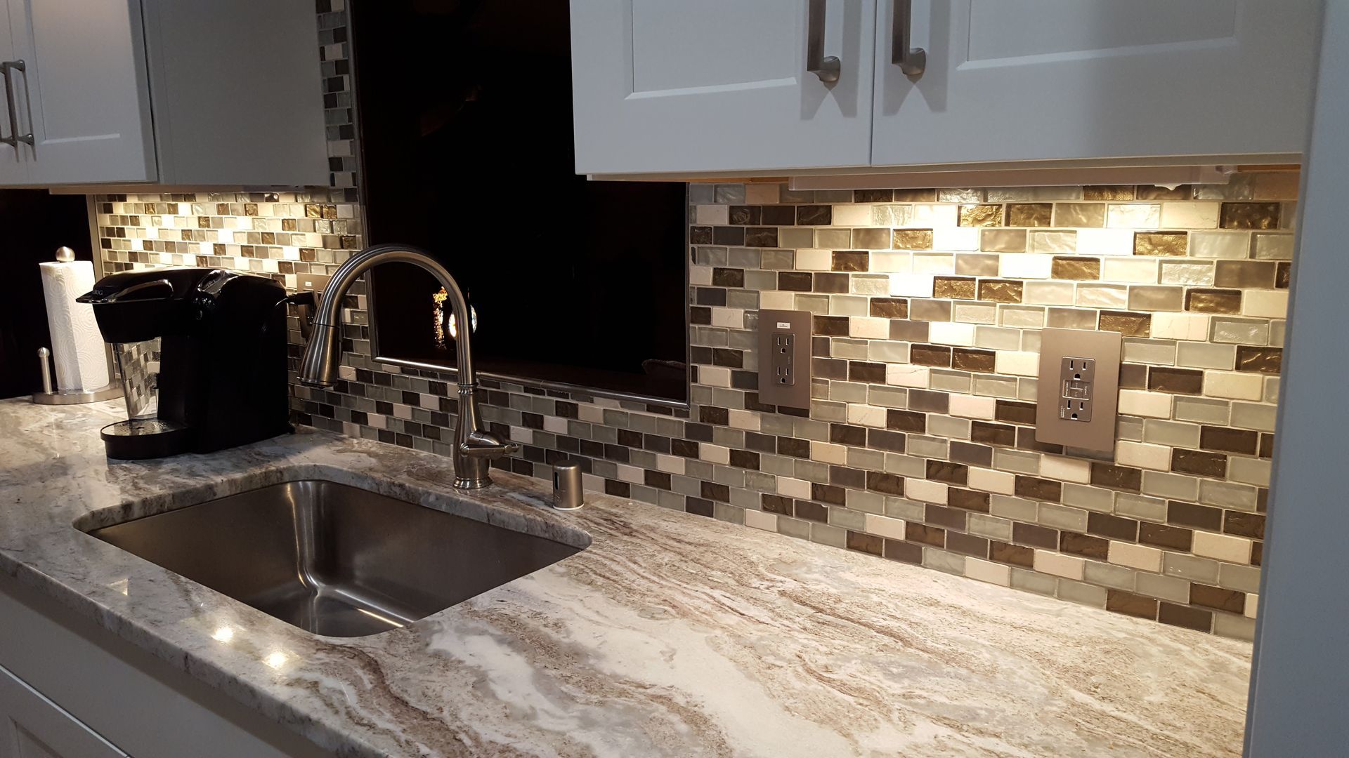 Kitchen sink with chrome faucet, mosaic tile backsplash, and speckled stone countertop