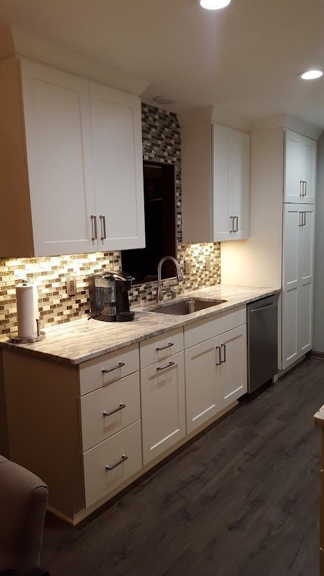 Modern kitchen with white cabinets, dark countertops, mosaic backsplash, and wood-look flooring.