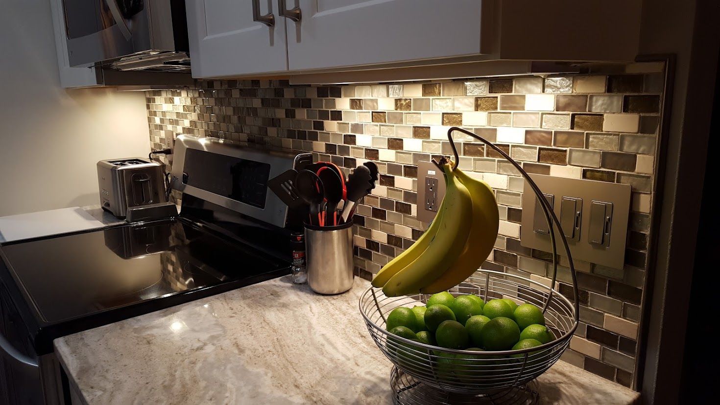 Modern kitchen countertop with mosaic backsplash, bananas, limes, knife block, and espresso machine.