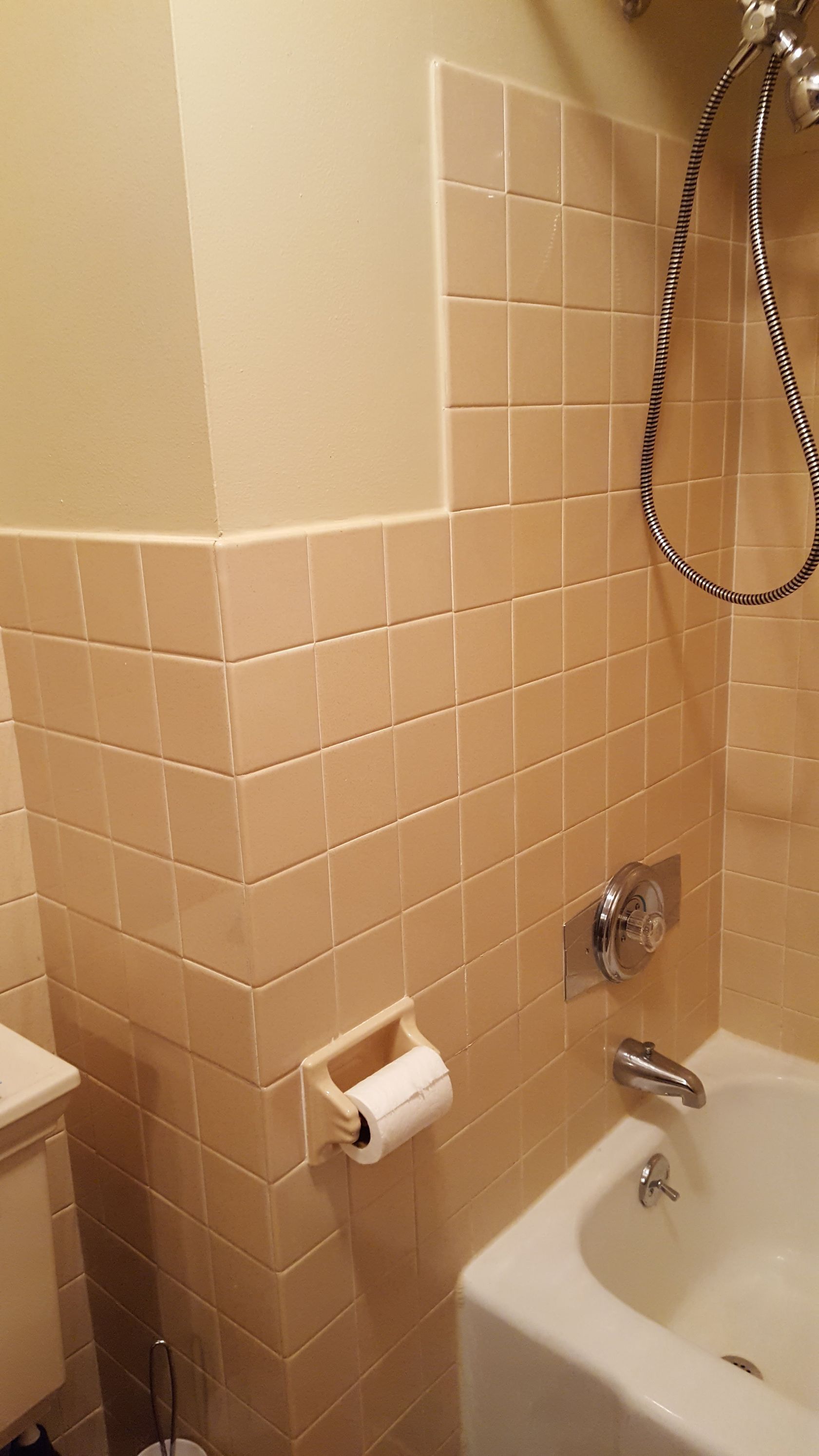 Small beige-tiled bathroom with a bathtub, shower hose, faucet, and toilet paper holder.