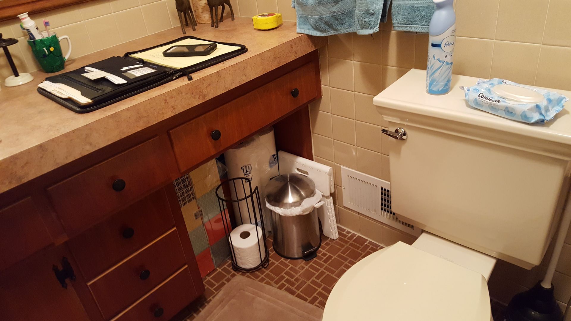 Bathroom with toilet, vanity, trash can, and cleaning supplies in a small tiled space