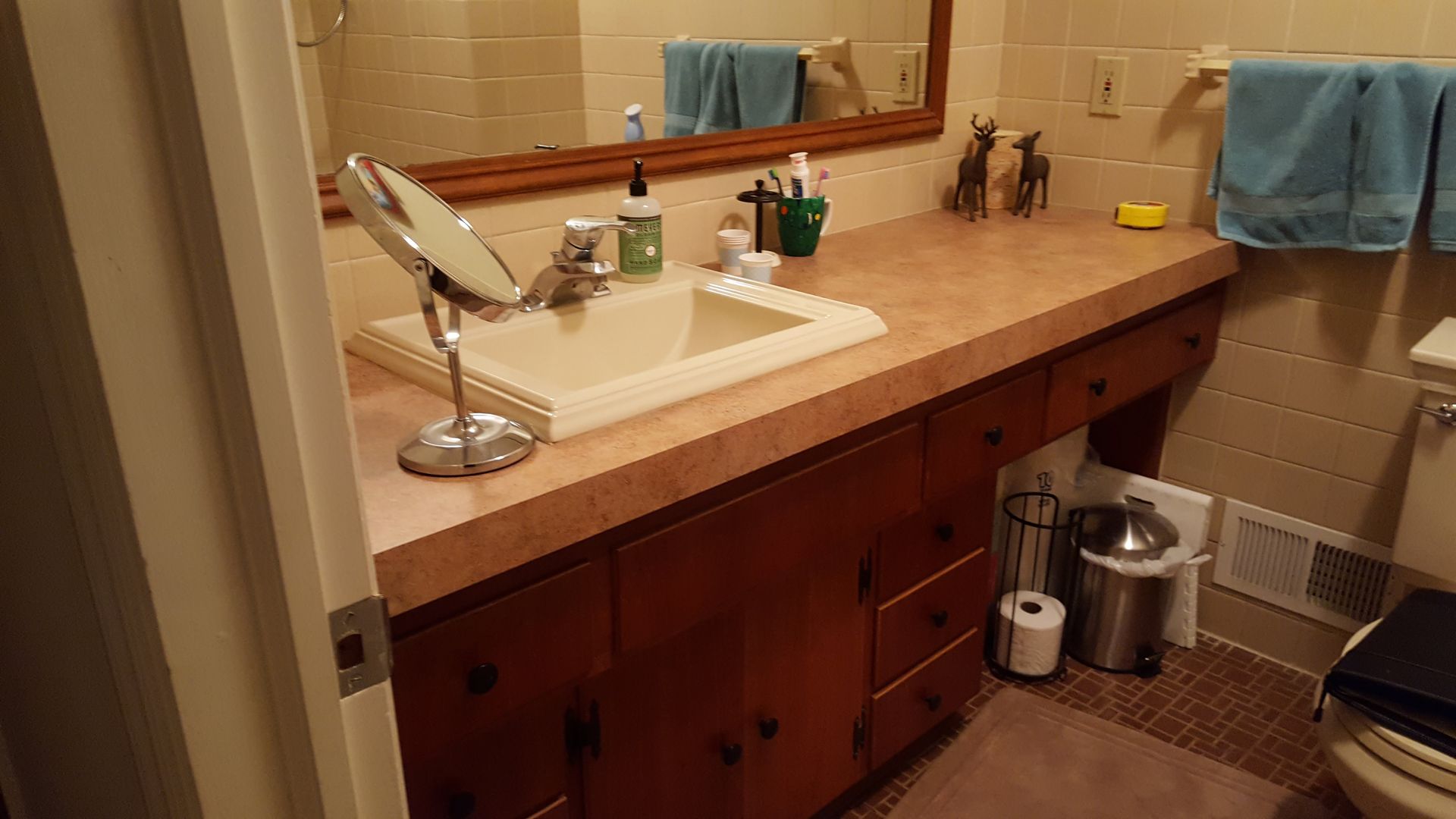 Bathroom vanity with brown countertop, sink, mirror, towels, and toiletries.