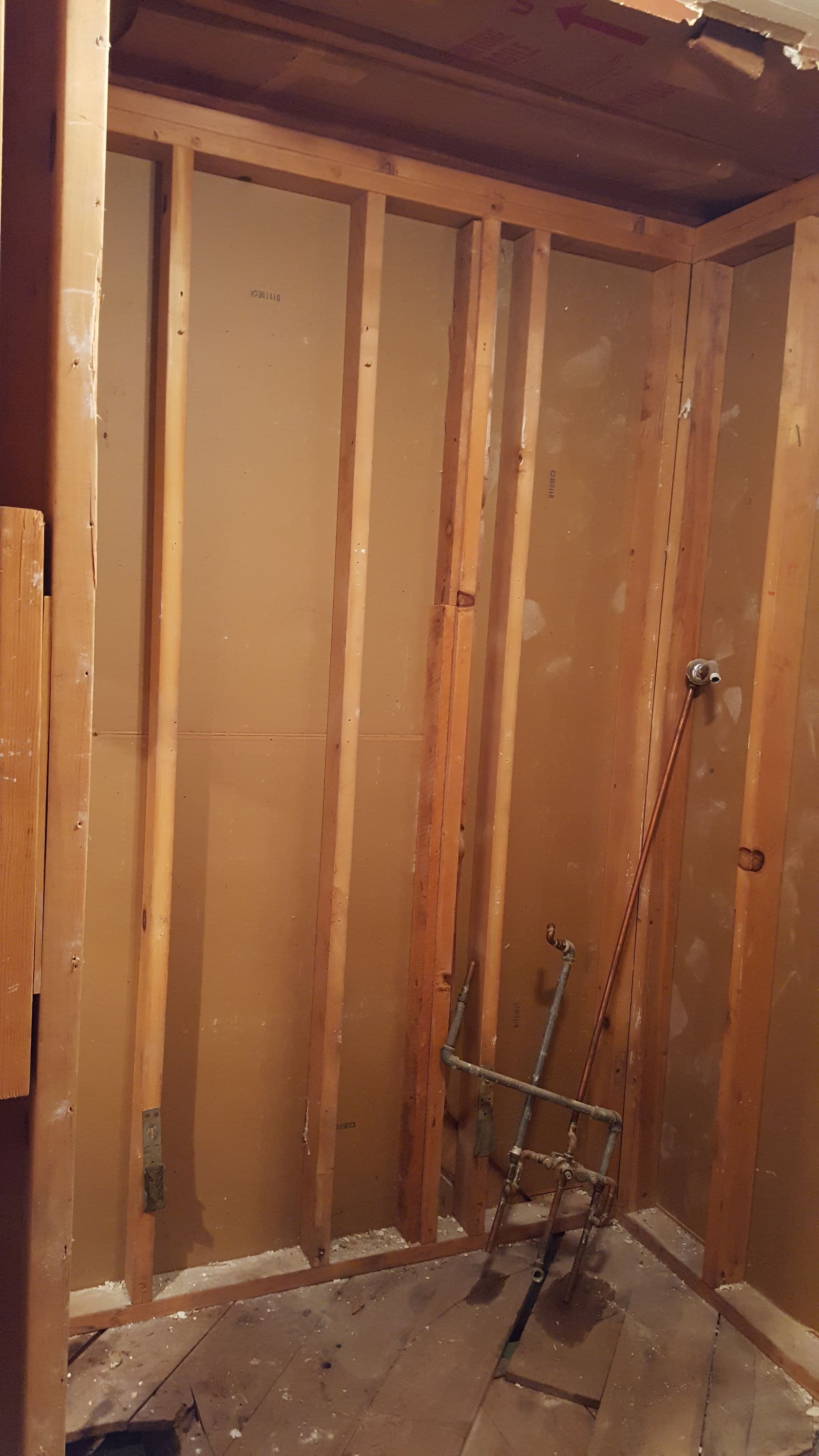 Interior wall studs in an unfinished room with exposed plumbing near the floor.