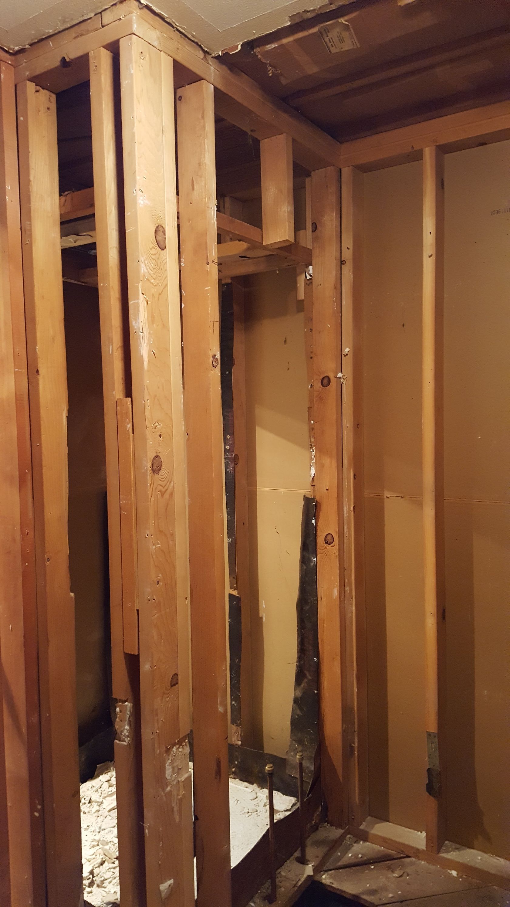 Exposed wooden wall studs and framing inside a room under construction, with debris on the floor.