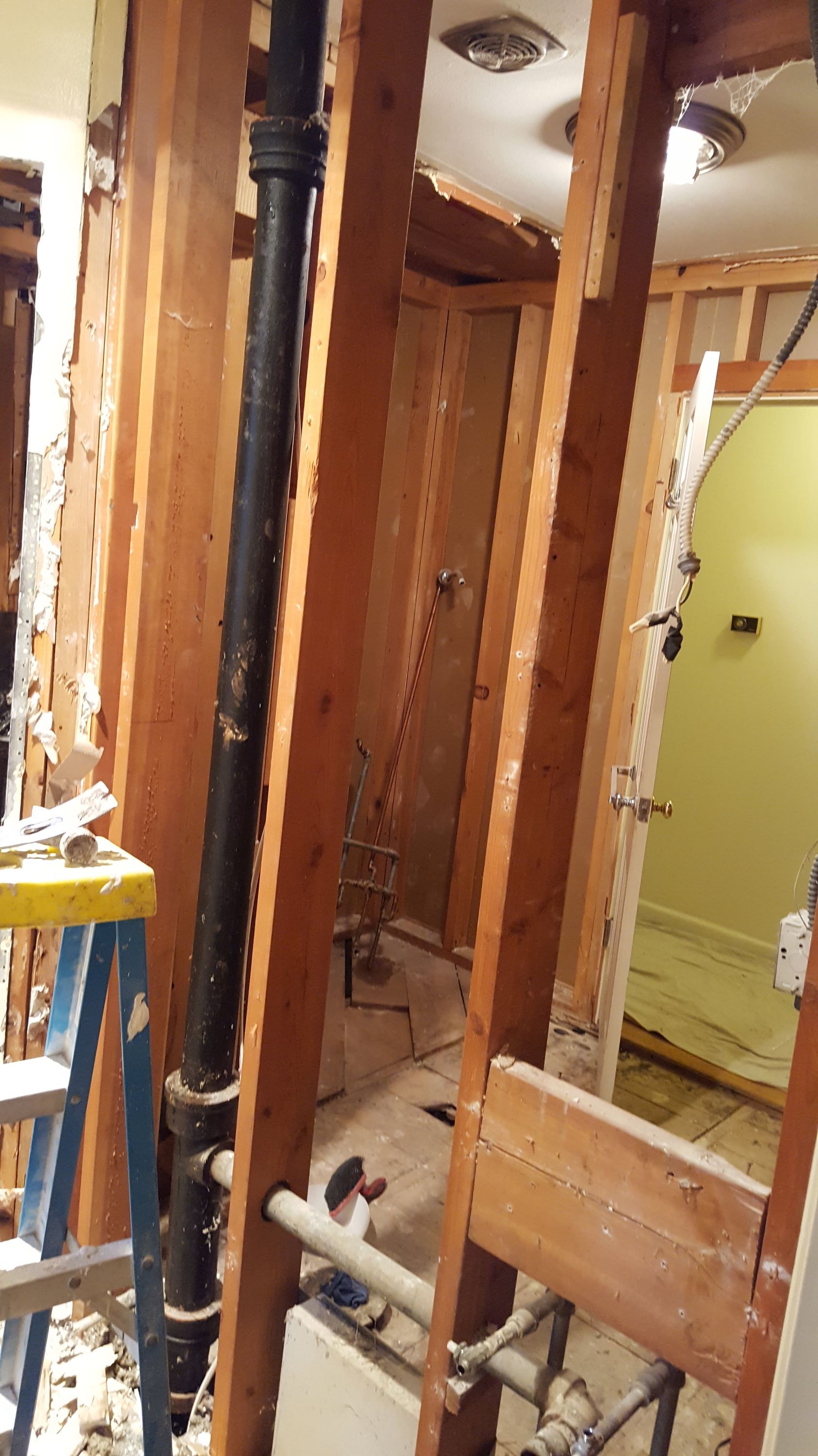 Partially demolished interior wall framing with exposed studs, pipes, and a doorway in a renovation site