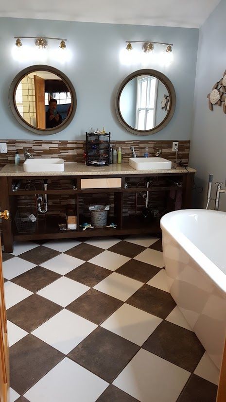Bathroom with double sink vanity, round mirrors, brown-and-white checkered floor, and a bathtub on the right.