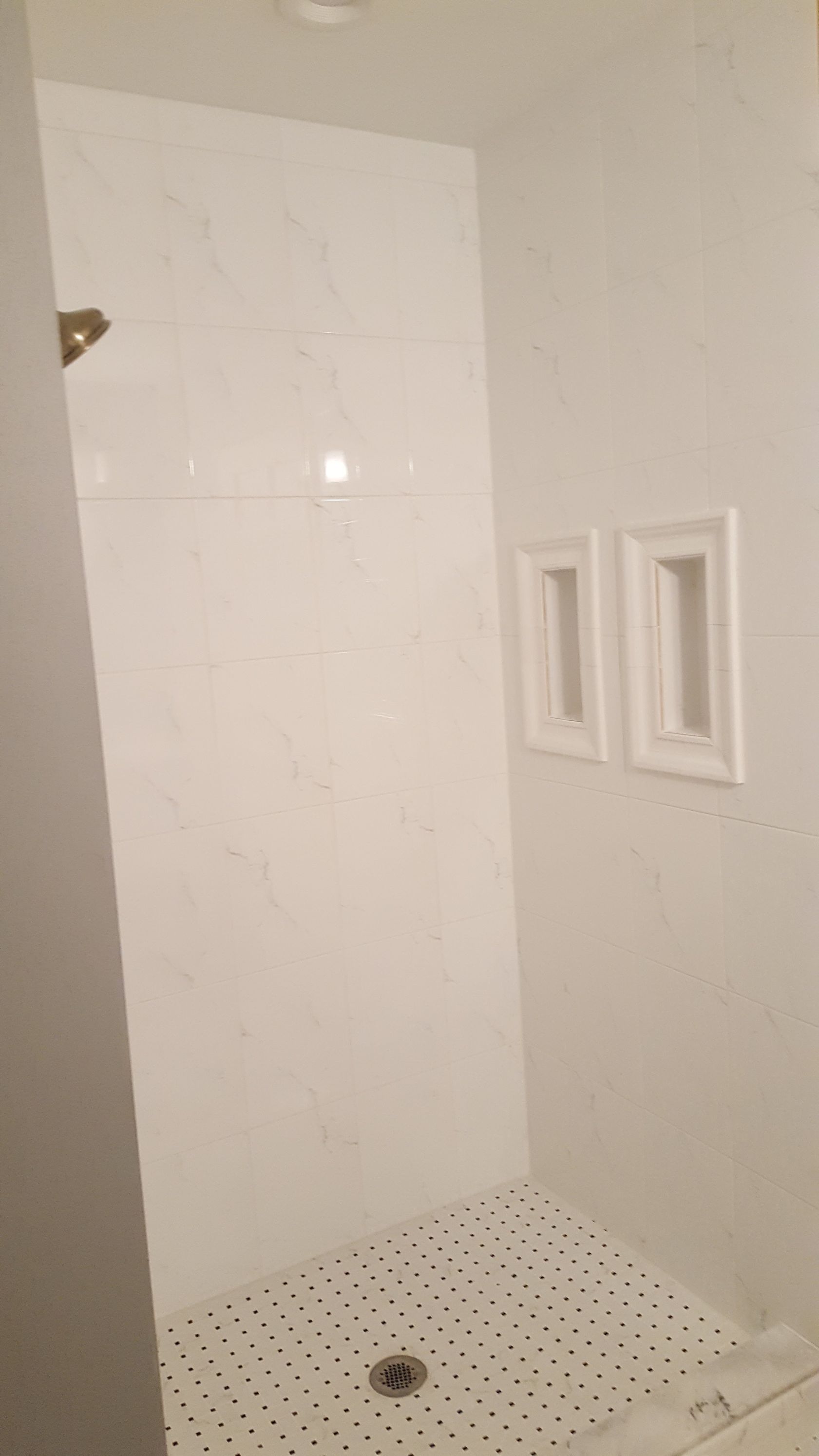 White tiled shower stall with a small shelf niche and a perforated shower floor drain.