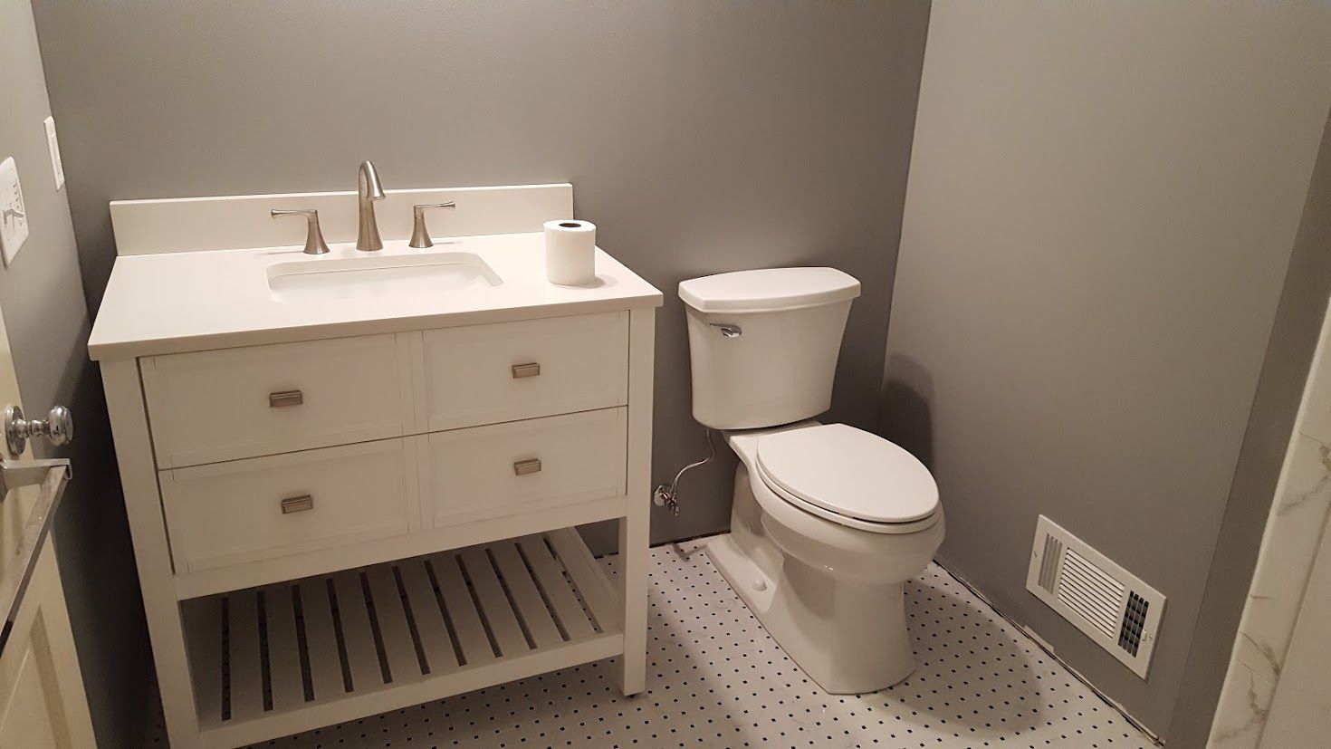 Small gray bathroom with white vanity, toilet, and patterned floor tiles