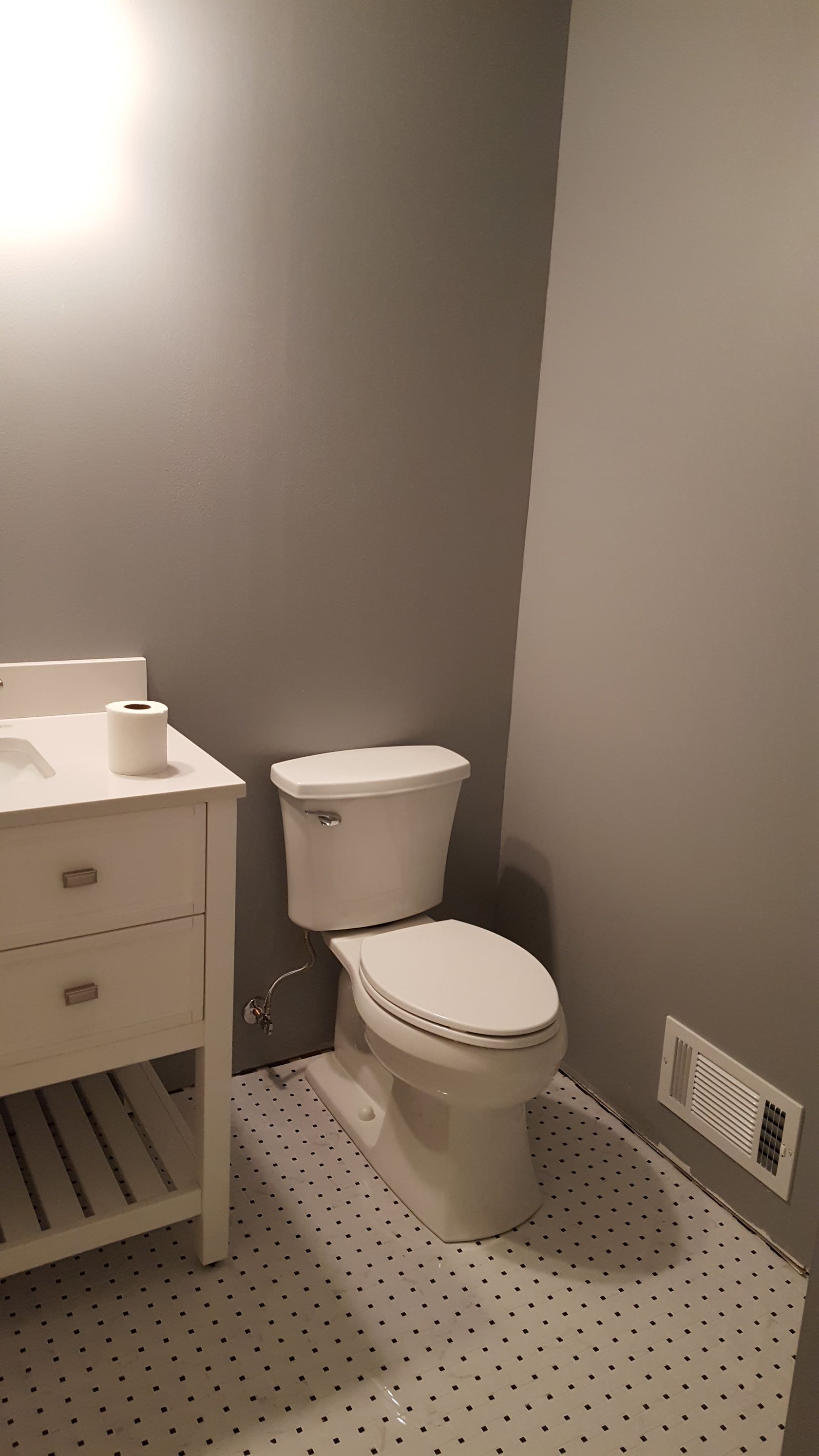 Small gray bathroom with a toilet, sink vanity, and patterned floor.