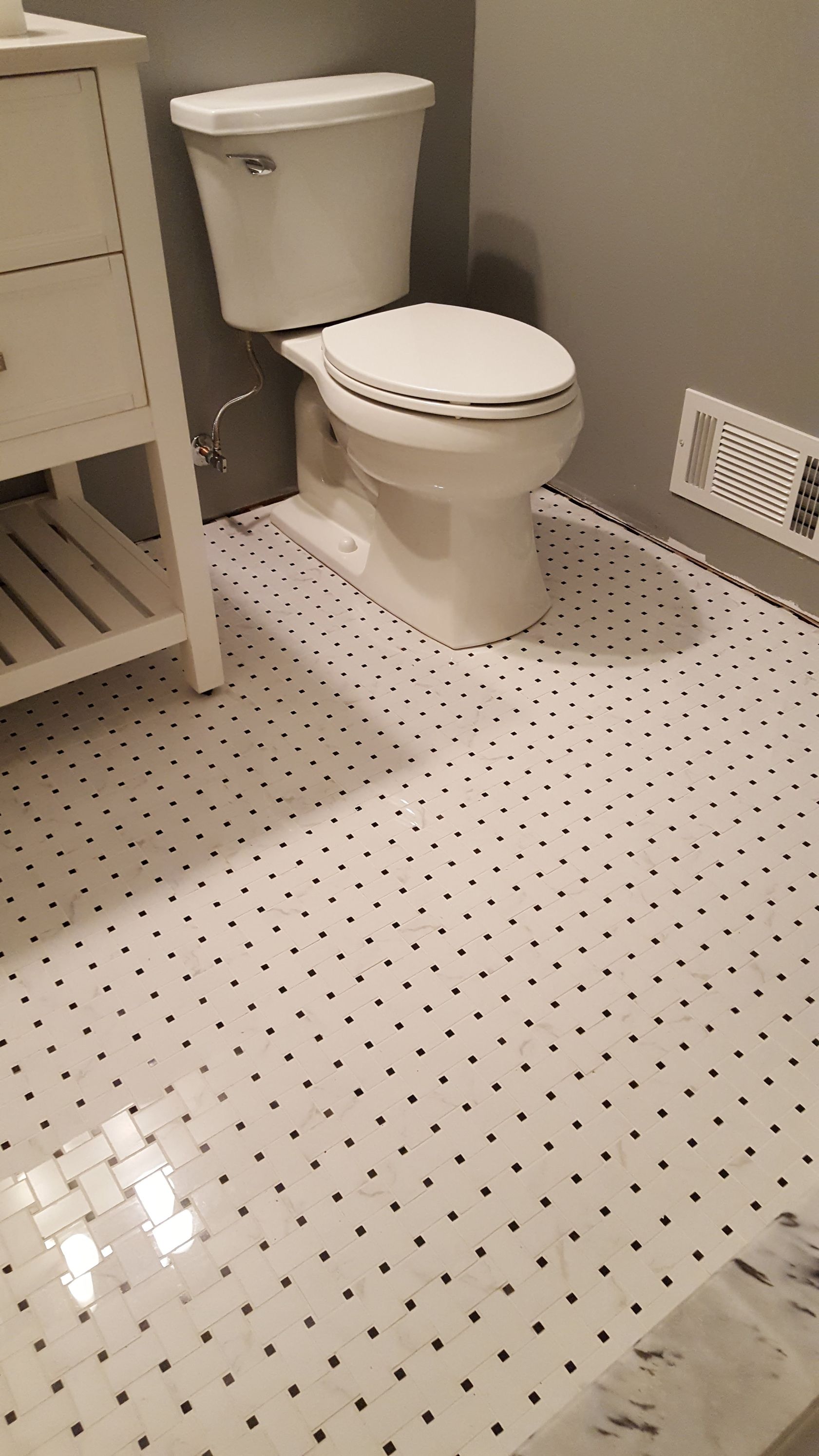 Small bathroom with white toilet, light gray walls, and white floor tiles with black dots.