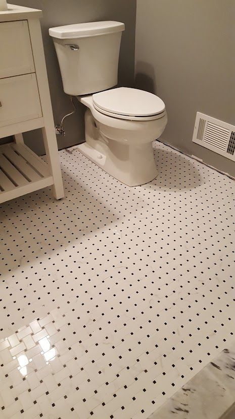 Small bathroom with white toilet and dotted tile floor near a wall vent.