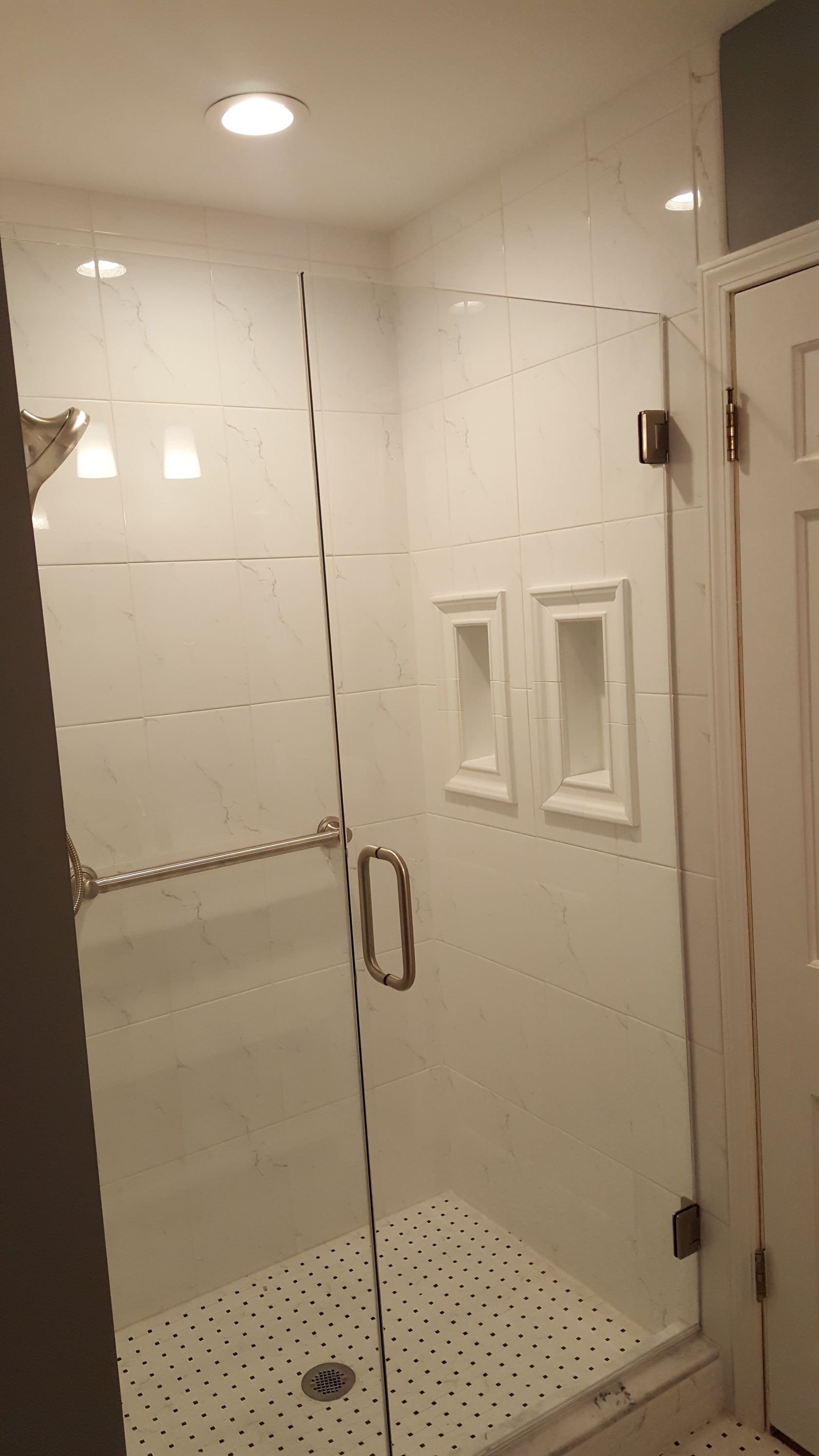 Glass shower with white tile walls, built-in shelves, and a pebble-style floor in a bright bathroom.