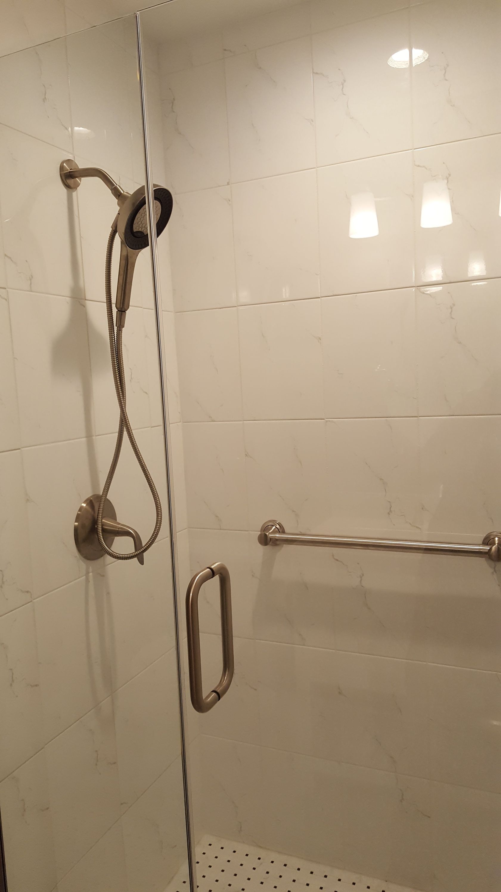 Shower stall with handheld showerhead, grab bars, and glass door in a tiled bathroom.