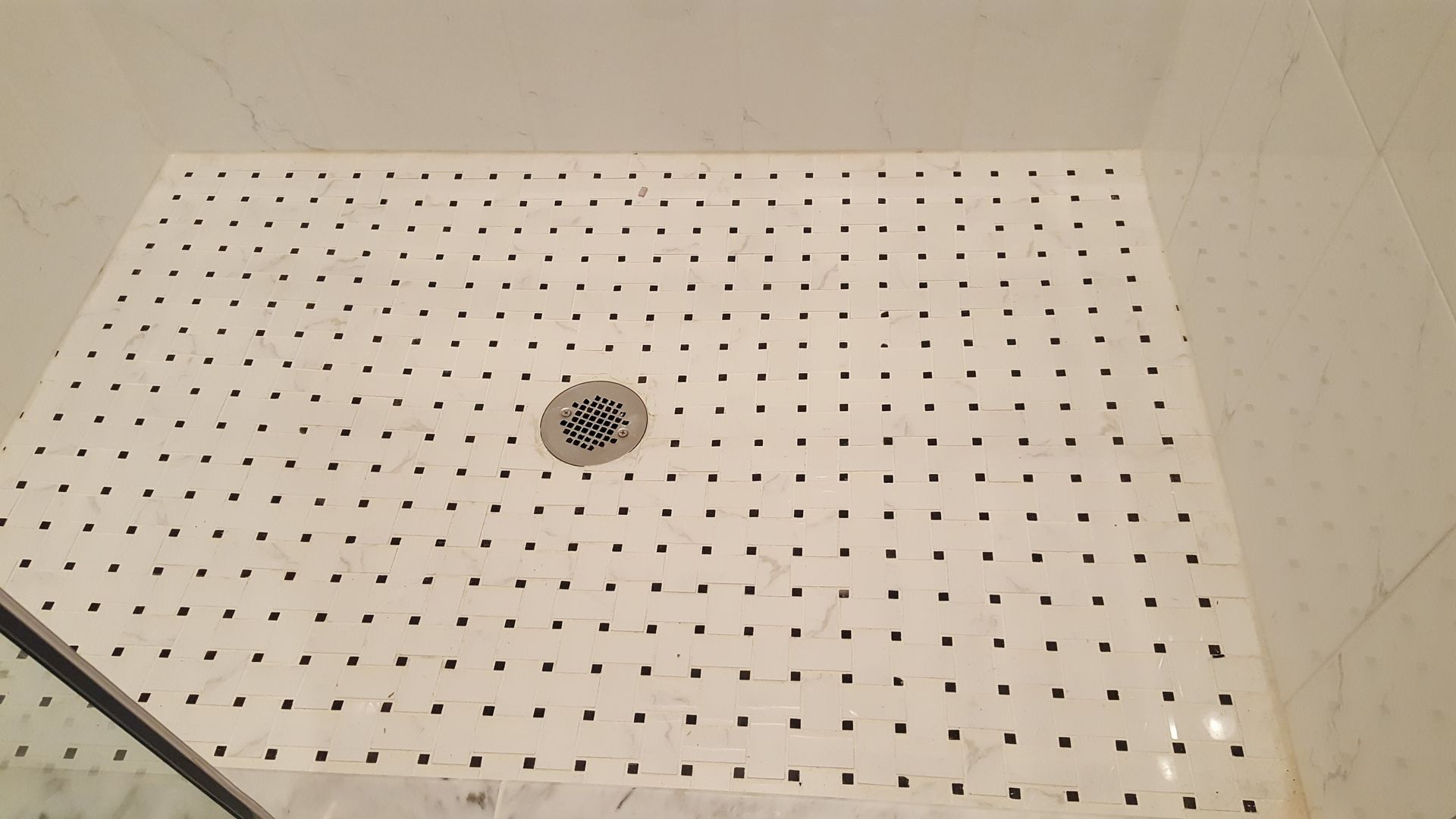 White tiled shower floor with a small round drain and black dot pattern